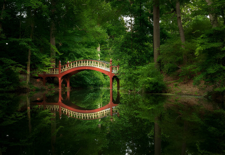 Ornate wooden bridge over very calm Crim Dell pond on campus of William and Mary college in Williamsburg Virginia