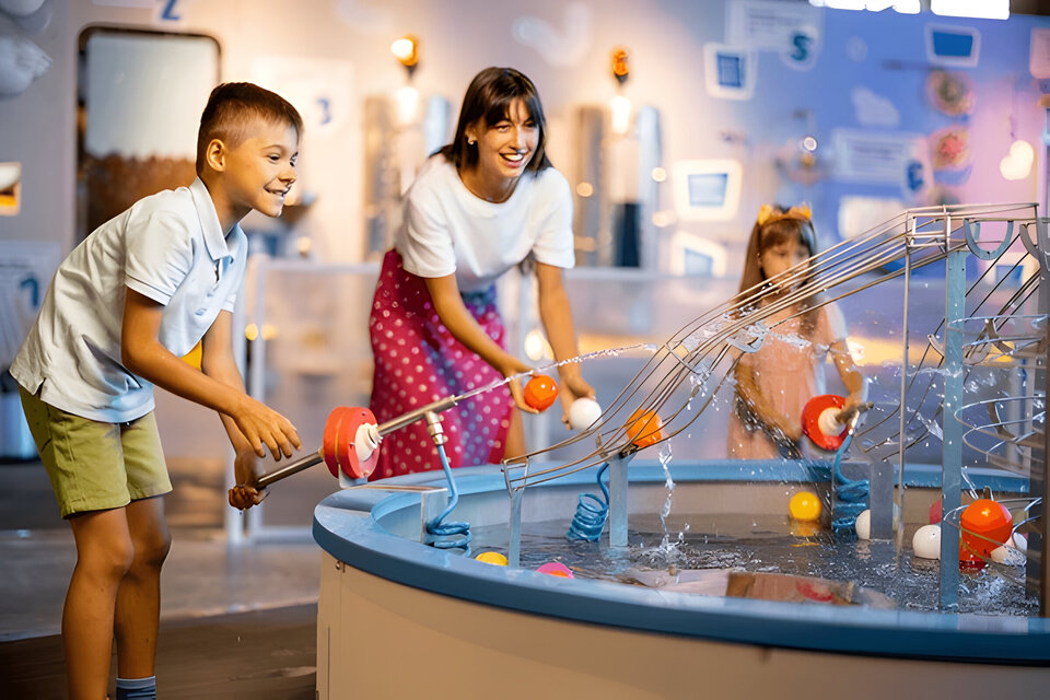 Mom with kids play with balls, learning physical phenomena in an interesting way, having fun in a science museum with interactive models